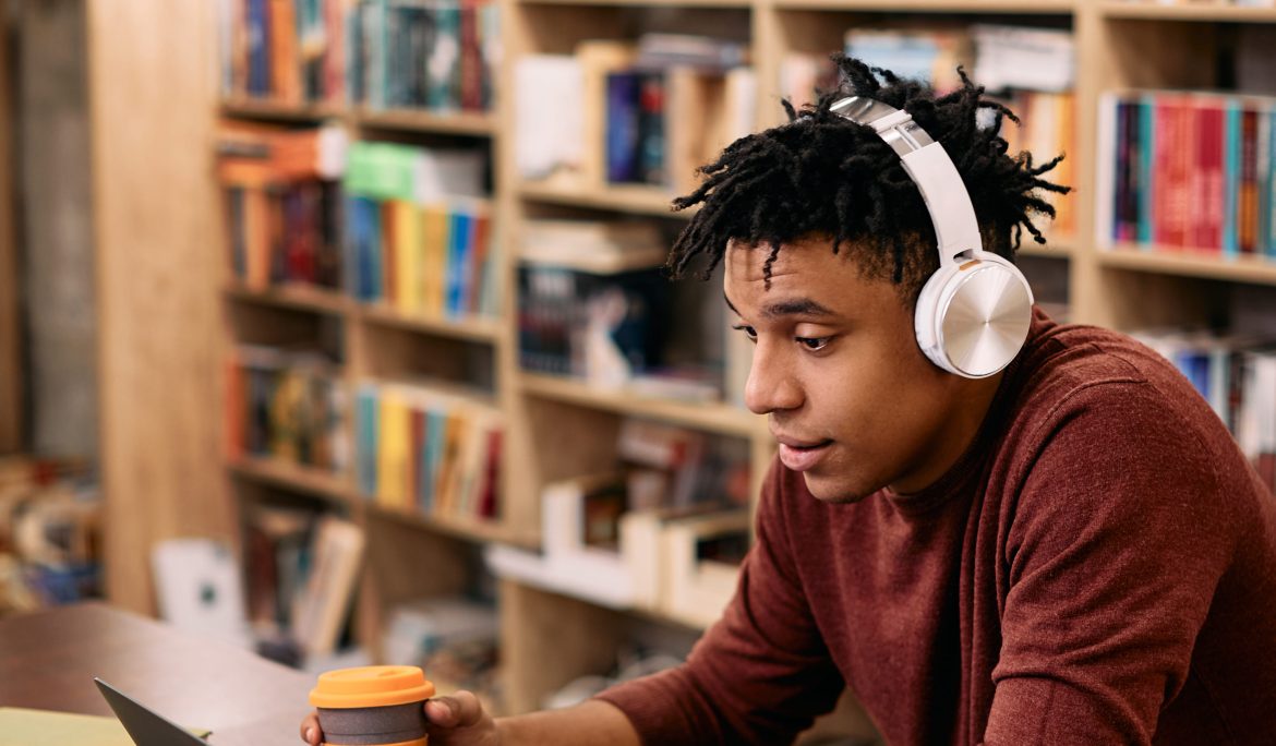 College student with headphones studying on a laptop in a library café