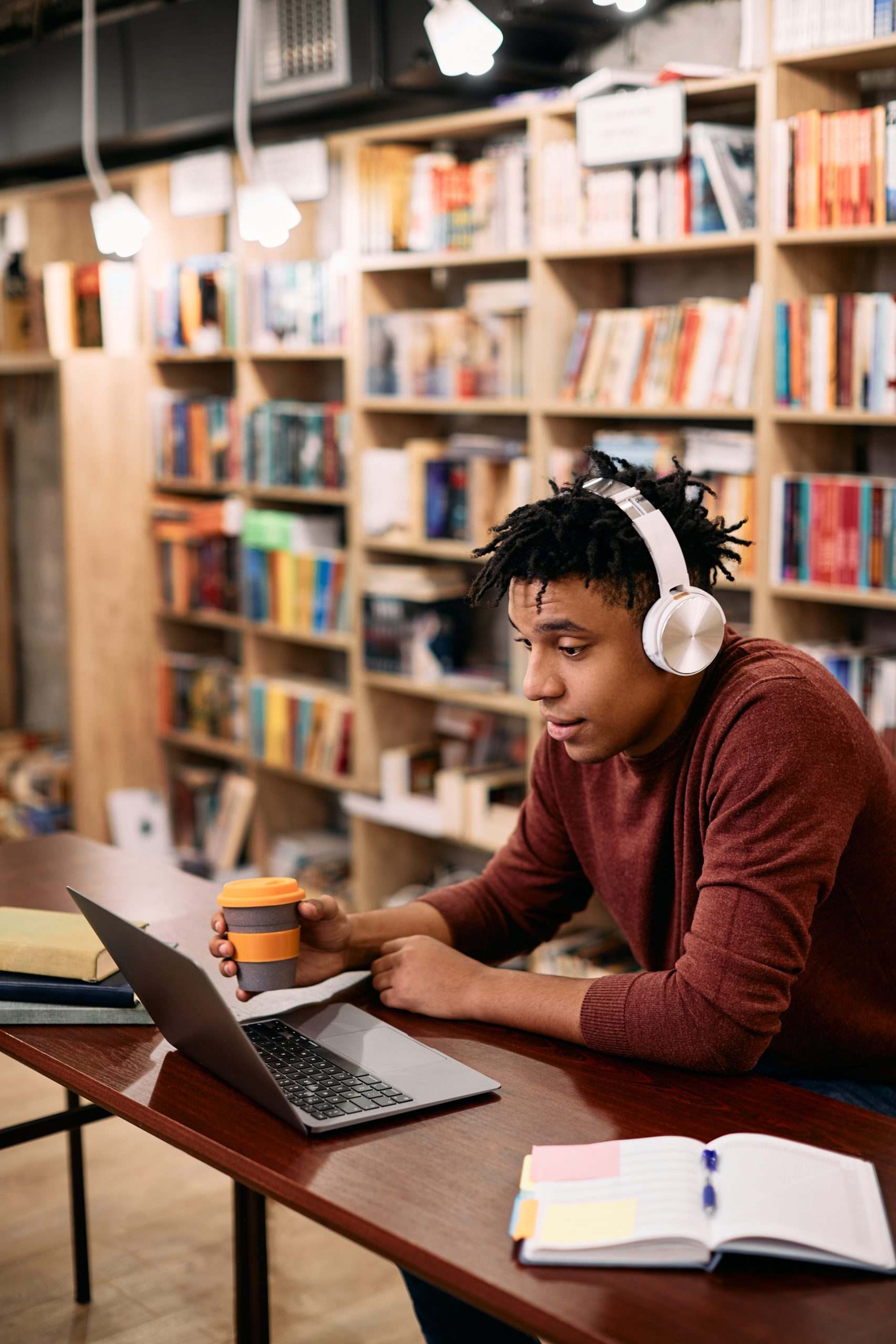 College student with headphones studying on a laptop in a library café