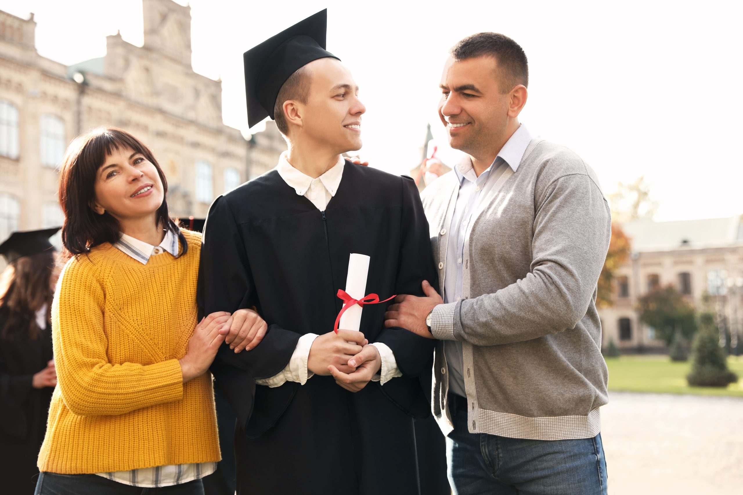 Graduate in cap and gown holding a diploma with his proud parents