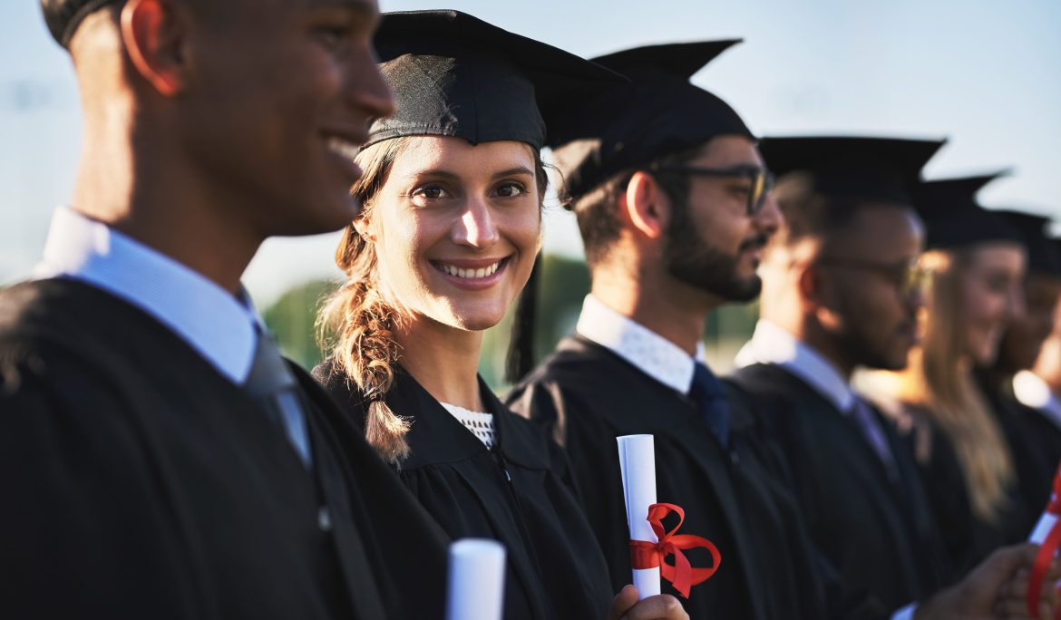 Smiling graduates in caps and gowns holding diplomas at a graduation ceremony