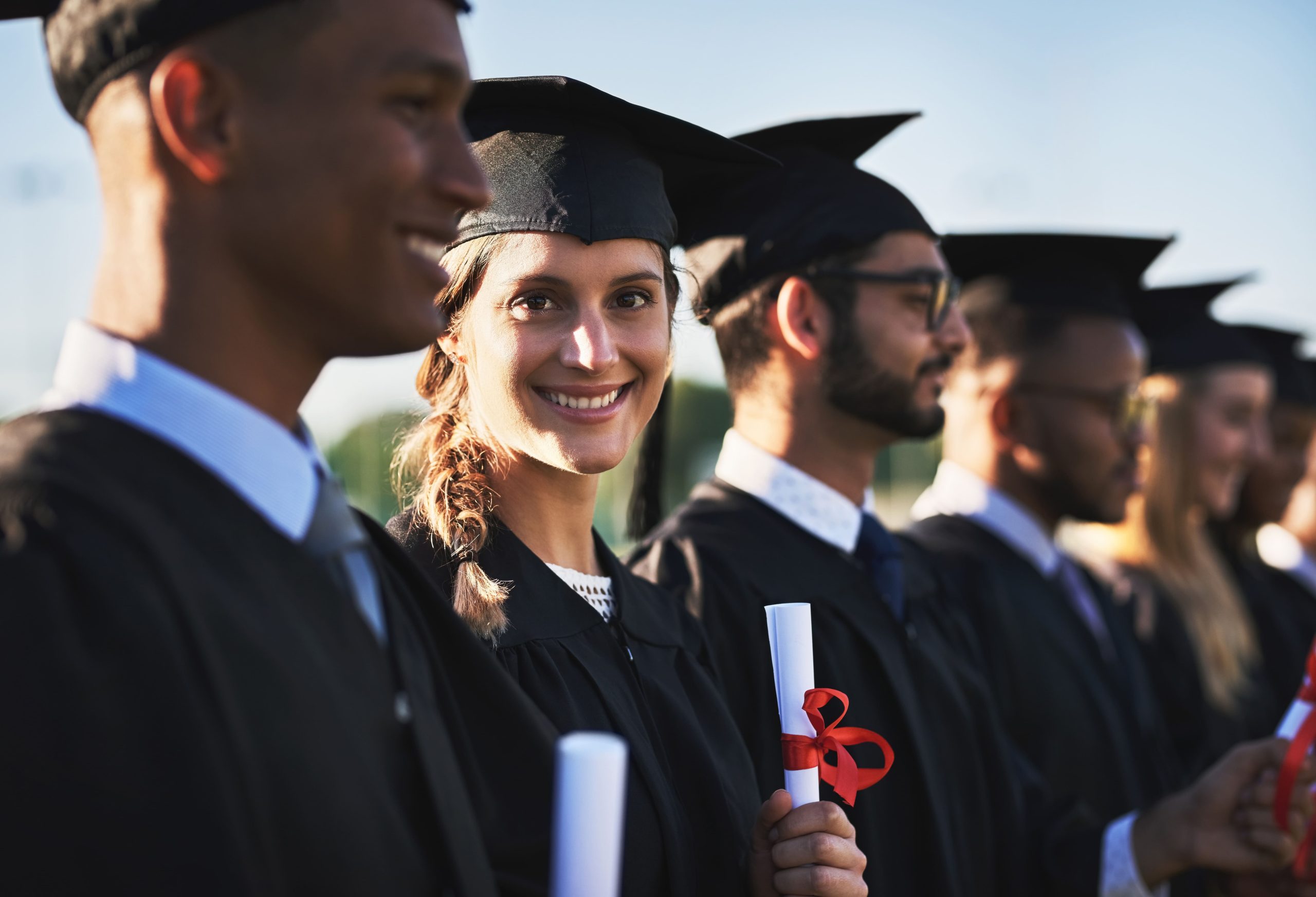 Smiling graduates in caps and gowns holding diplomas at a graduation ceremony