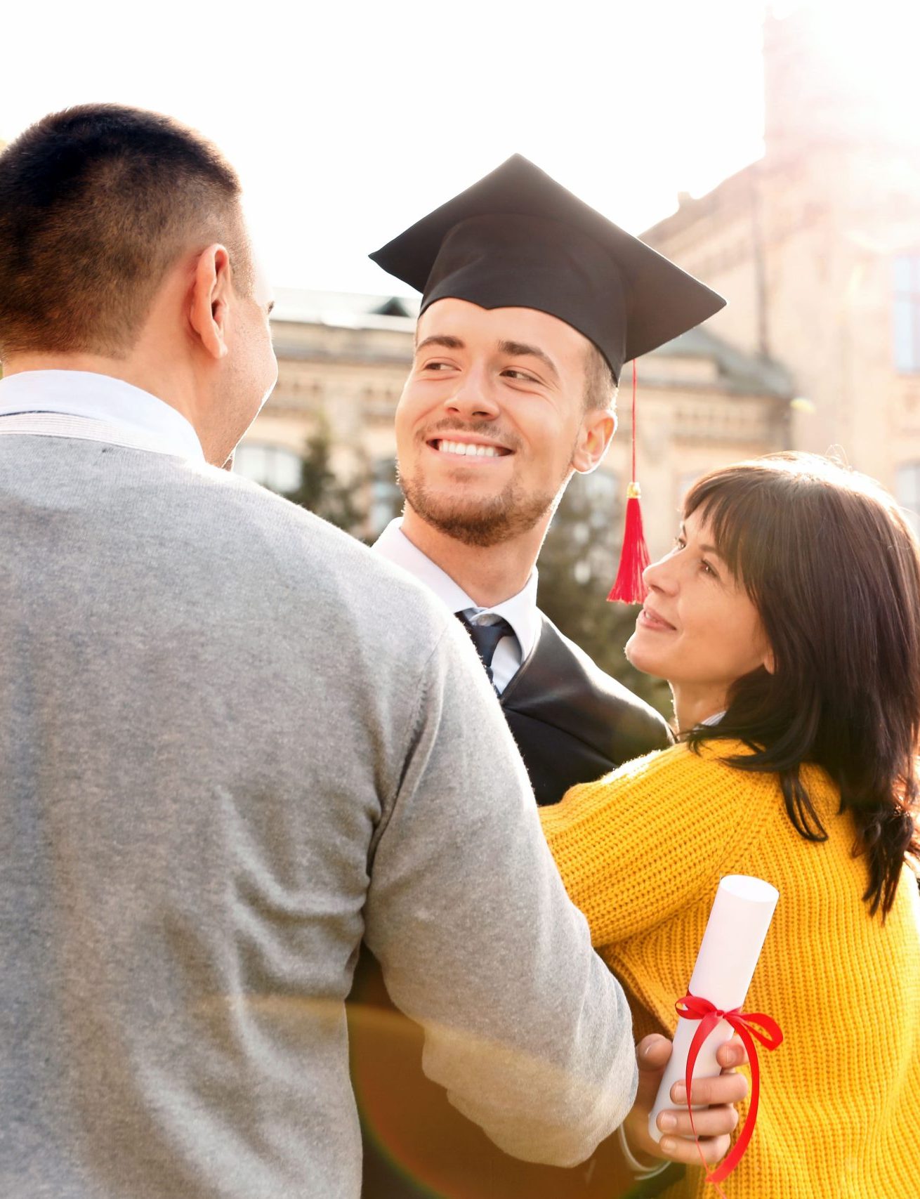 Graduate in cap and gown celebrating with his parents on a college campus