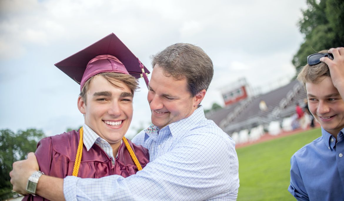 Proud father hugging his son in a graduation cap and gown