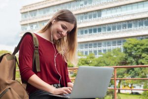 A college student smiling at her laptop on campus