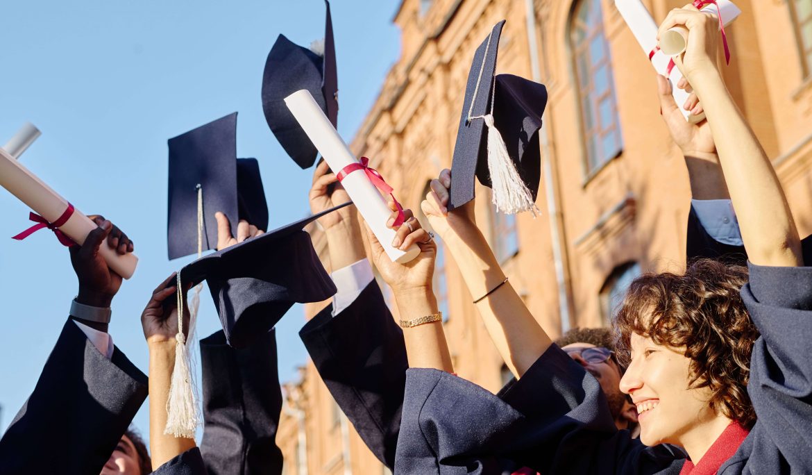 Graduates tossing their caps and holding diplomas in front of a university building