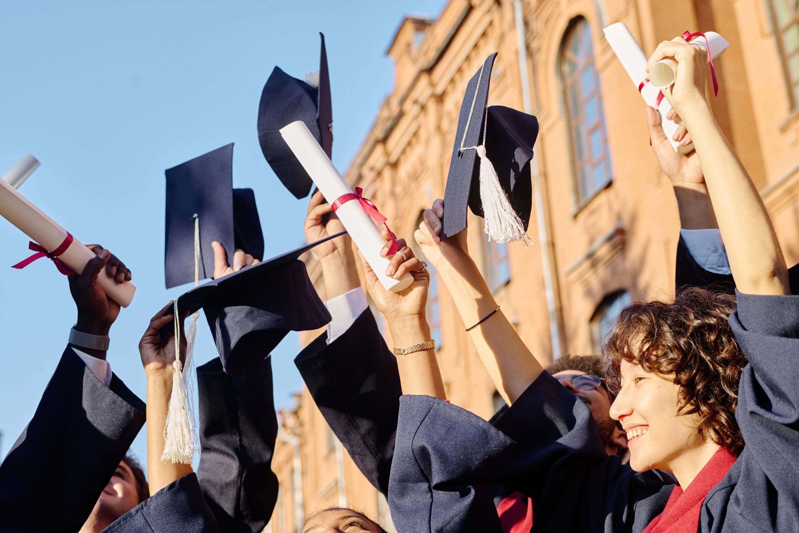 Graduates tossing their caps and holding diplomas in front of a university building