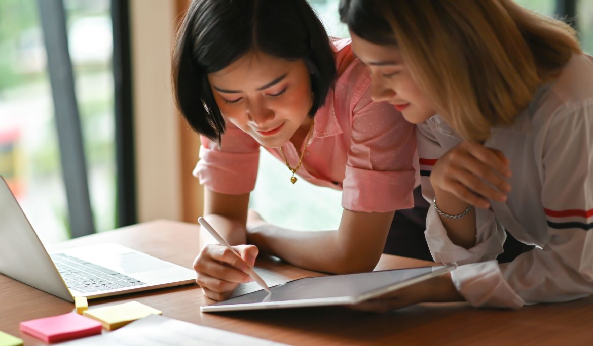 Two students collaborating on a tablet and laptop at a desk