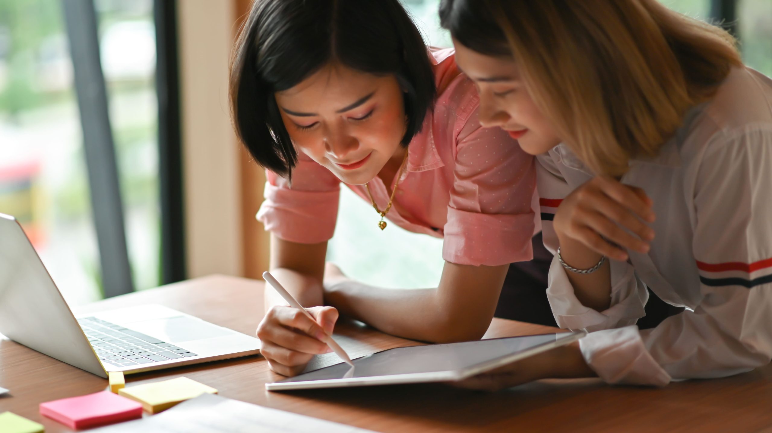 Two students collaborating on a tablet and laptop at a desk